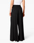 A model from the back wearing black wide-leg pants with an elastic waistband, paired with a white top, against a clean white studio background.