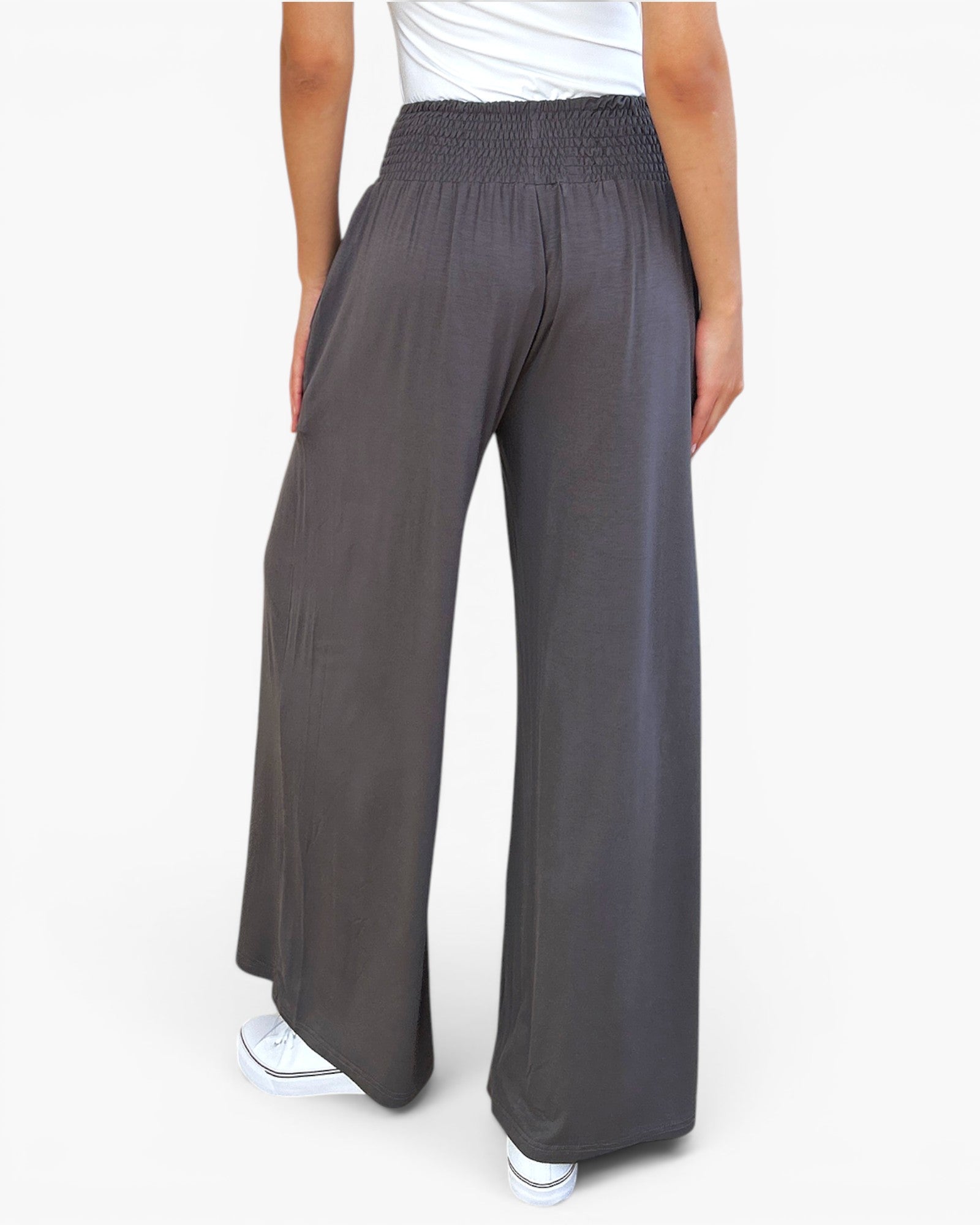 A person wearing loose, wide-leg dark gray pants with a smocked elastic waistband, shown from the back against a plain white studio background.