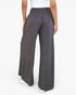 A person wearing loose, wide-leg dark gray pants with a smocked elastic waistband, shown from the back against a plain white studio background.