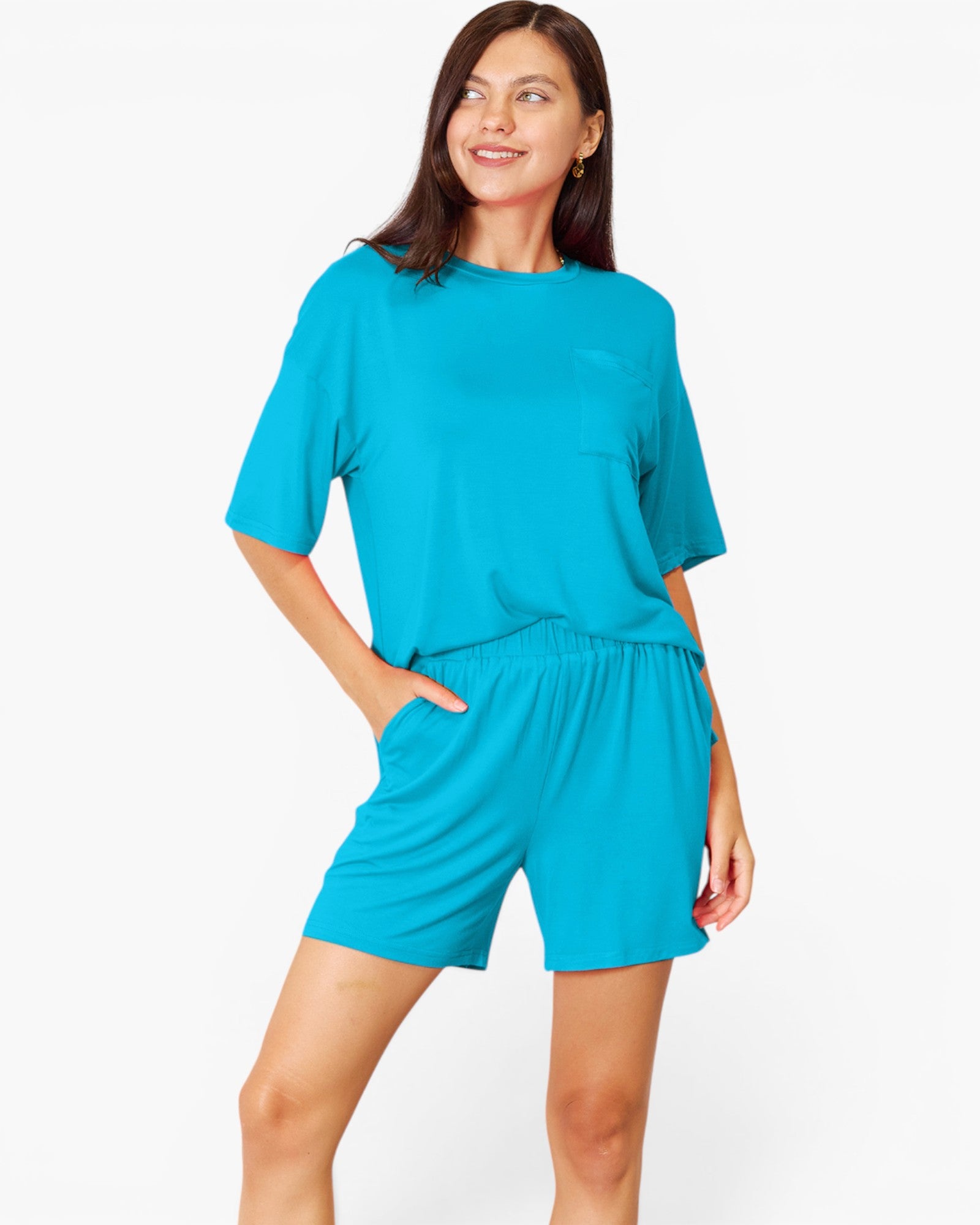 A woman modeling a bright turquoise blue lounge set consisting of a short-sleeve crewneck top and matching shorts, set against a plain white studio background.