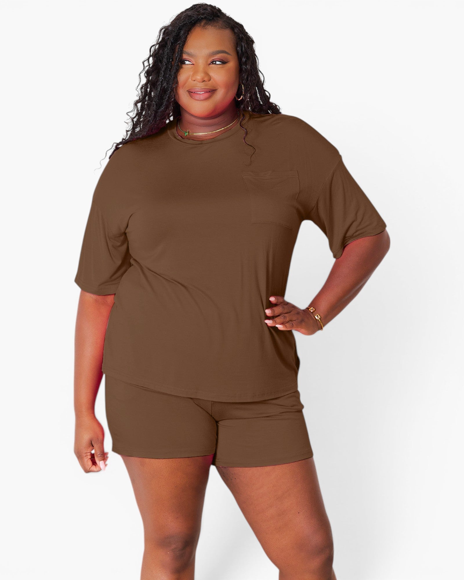 A woman modeling a matching brown short-sleeve crewneck top and shorts set against a plain light gray studio background.