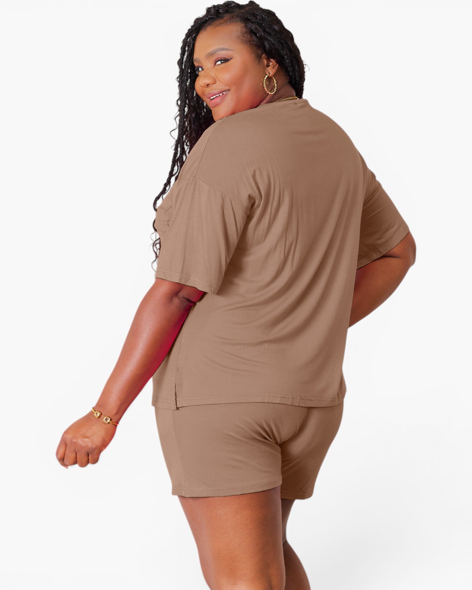 A woman modeling a matching two-piece lounge set in a warm taupe-brown color, featuring a short-sleeve top and shorts, shown from a three-quarters back view against a plain white background.