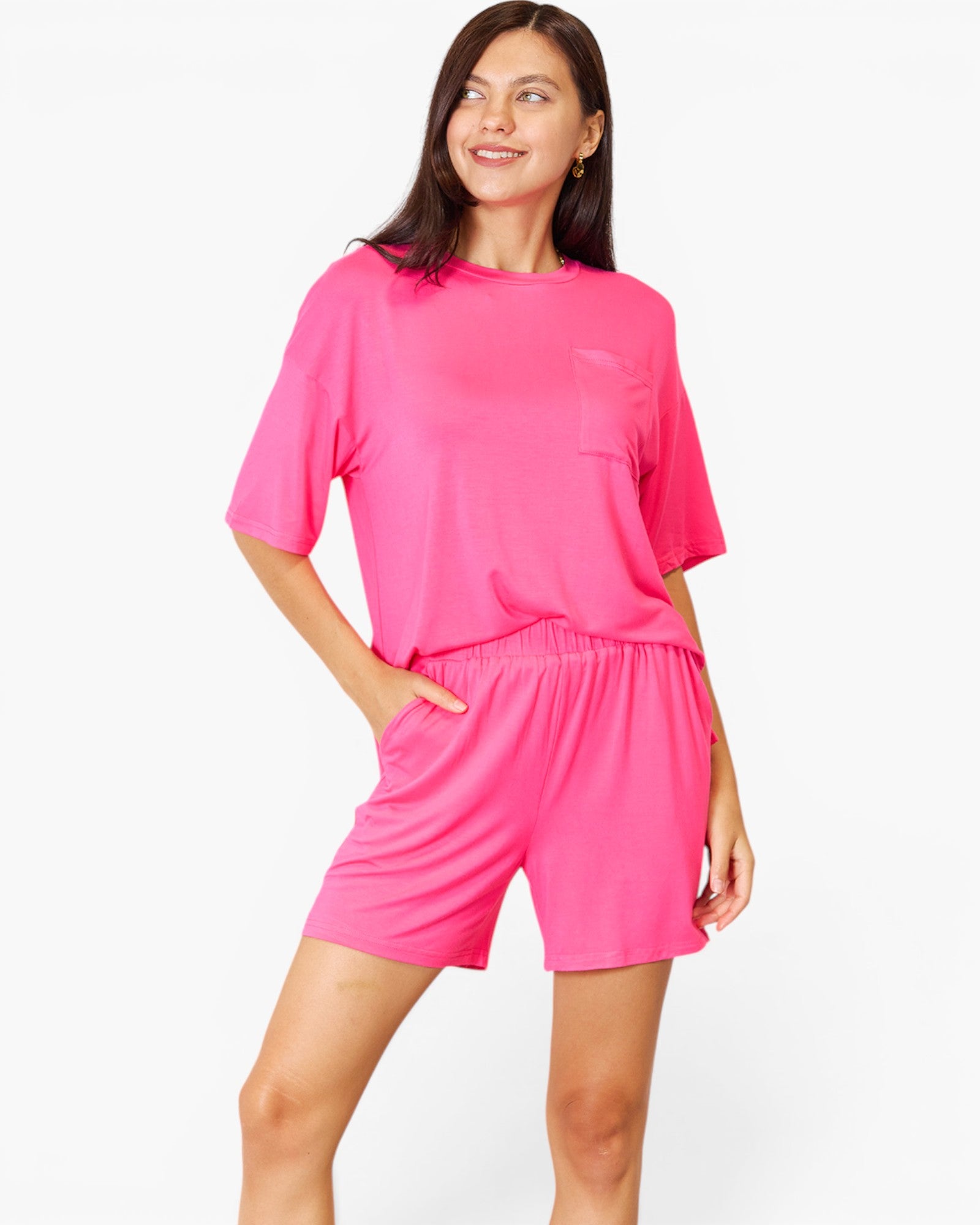 A woman modeling a bright pink lounge set consisting of a short-sleeve crewneck top and matching shorts against a plain white studio background.