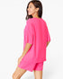 A woman modeling a bright pink lounge set consisting of an oversized short-sleeve top and matching shorts, shown from a three-quarters back view against a plain white studio background.