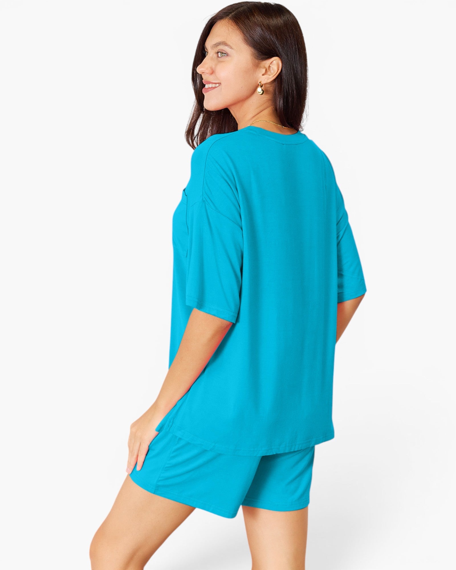 A woman wearing a bright turquoise blue short-sleeve top and matching shorts, shown from a side-back angle against a clean white studio background.