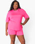 A woman modeling a bright pink matching lounge set consisting of a short-sleeve crewneck t-shirt with a chest pocket and matching shorts, against a plain white studio background.