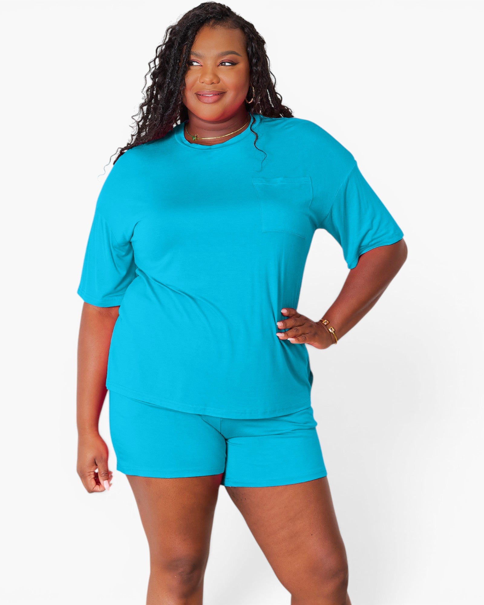 A woman modeling a bright turquoise blue short-sleeve top and matching shorts against a clean white studio background.