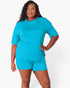 A woman modeling a bright turquoise blue short-sleeve top and matching shorts against a clean white studio background.