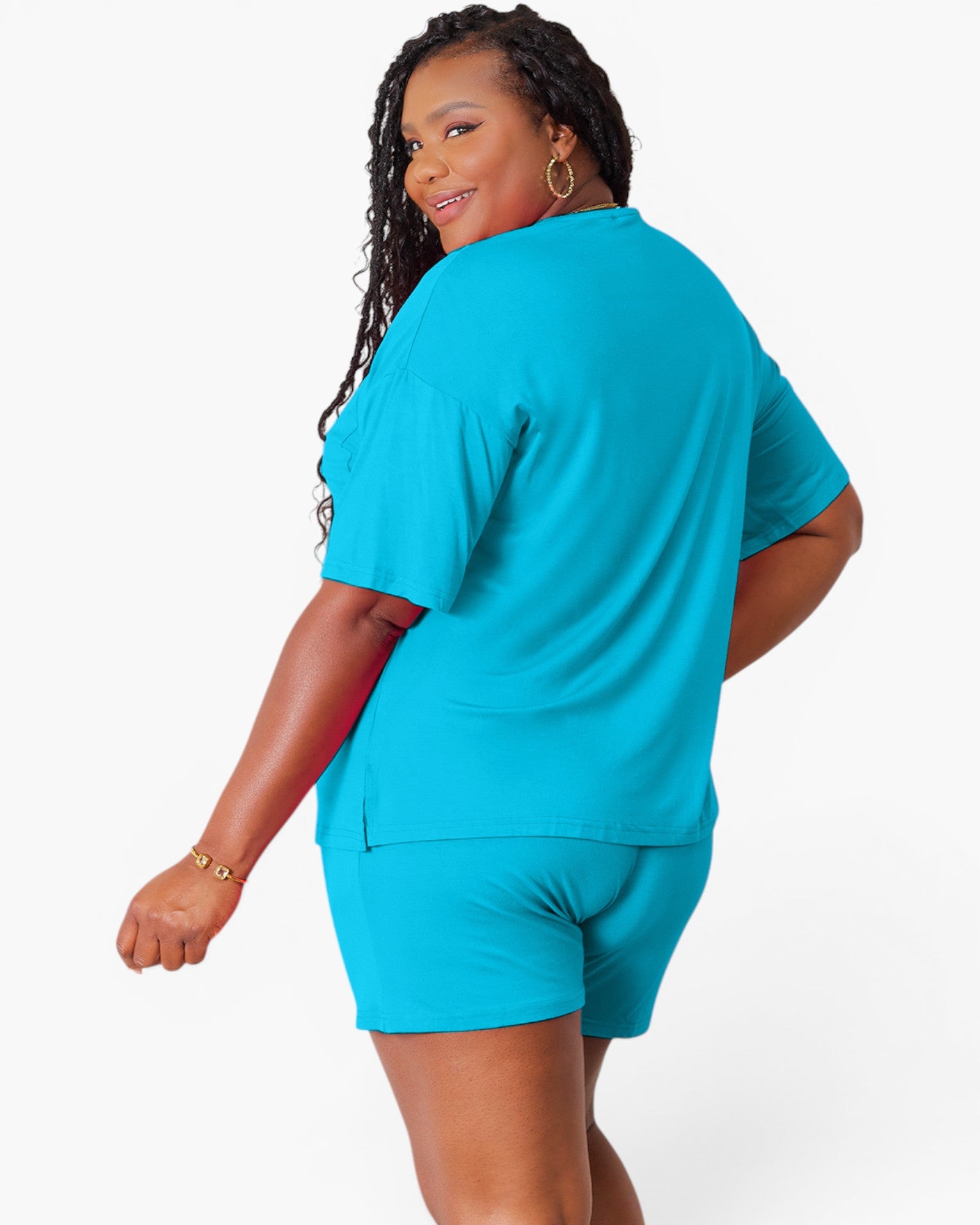A woman modeling a bright turquoise blue matching lounge set consisting of a short-sleeve top and shorts, shown from a three-quarters back view against a plain white studio background.
