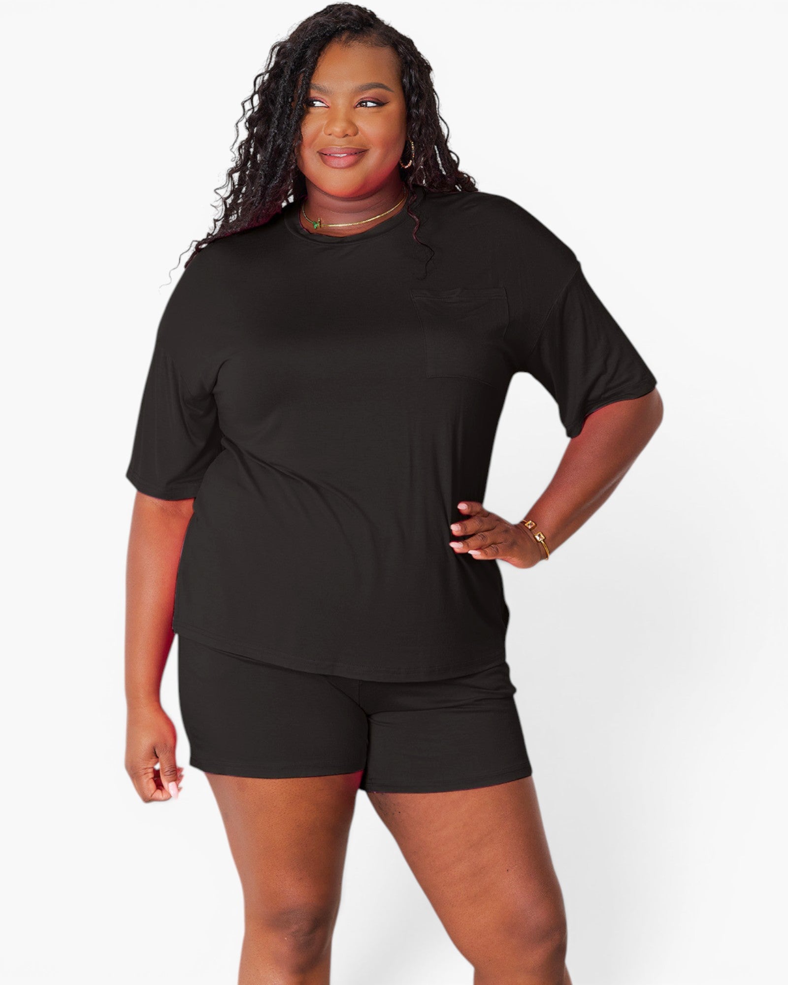 A plus-size woman modeling a black short-sleeve athletic t-shirt and matching black shorts against a light gray studio background.