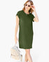 A woman modeling a short-sleeve olive green t-shirt dress, holding a small beige woven backpack against a plain white background.