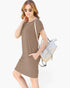 A woman modeling a short-sleeve taupe brown knit dress with side pockets, styled with a light-colored woven shoulder bag and sunglasses against a plain white background.
