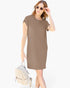 A woman modeling a short-sleeve, crew-neck knit dress in a solid taupe-brown color, styled with round sunglasses and a small woven cream backpack against a plain white background.
