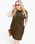 A woman modeling a short-sleeve, knee-length olive green dress with side pockets, styled with sunglasses and a brown crossbody bag against a plain white background.