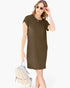 A woman modeling a short-sleeve, knee-length olive brown dress, styled with a light beige woven backpack and sunglasses, against a plain white background.