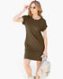 A woman modeling a short-sleeve, knee-length olive brown t-shirt dress, styled with sunglasses, a light-colored woven handbag, and white sneakers against a plain white background.