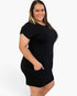 A woman modeling a black short-sleeve mini dress with a crew neck and side pockets, photographed against a plain light gray studio background.