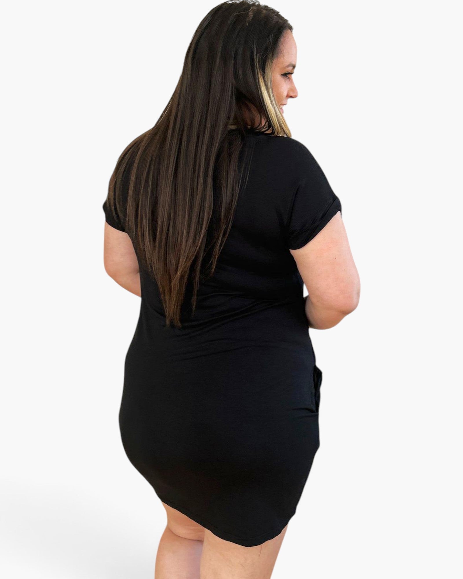 A woman with long dark brown hair is shown from the back wearing a black short-sleeve bodycon mini dress against a light gray studio background.