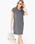 A woman modeling a short-sleeve gray t-shirt dress, holding a small beige woven backpack, against a plain white background.