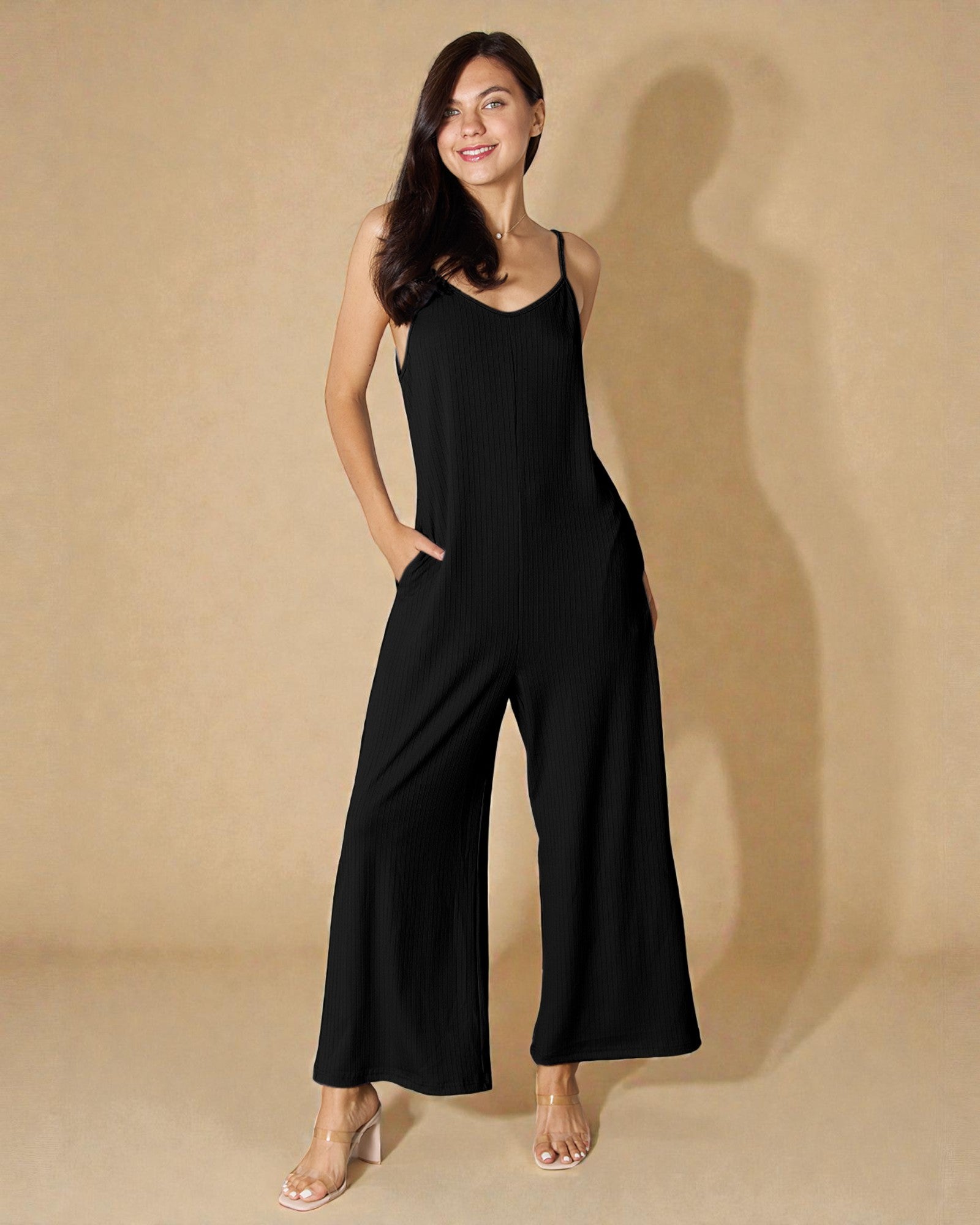 Woman wearing a black jumpsuit against a beige background