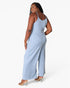 A woman modeling a light blue ribbed sleeveless jumpsuit from the back, standing against a plain white studio background.