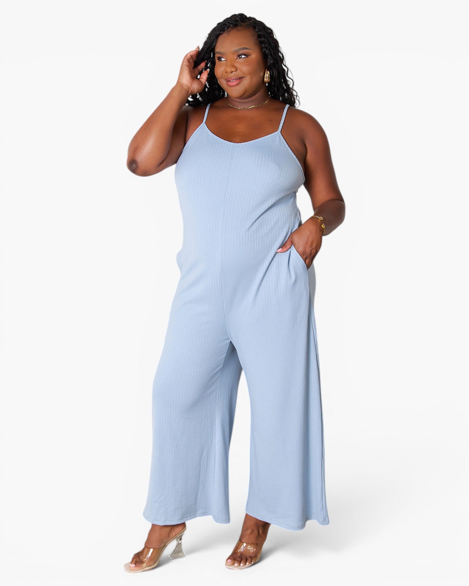 A woman modeling a light blue sleeveless jumpsuit with wide legs and thin shoulder straps, standing against a plain white studio background.