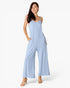 A woman modeling a light blue sleeveless jumpsuit with wide legs and thin shoulder straps, standing against a plain white studio background.