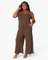 A woman modeling a sleeveless wide-leg jumpsuit in solid brown, standing against a clean white studio background.