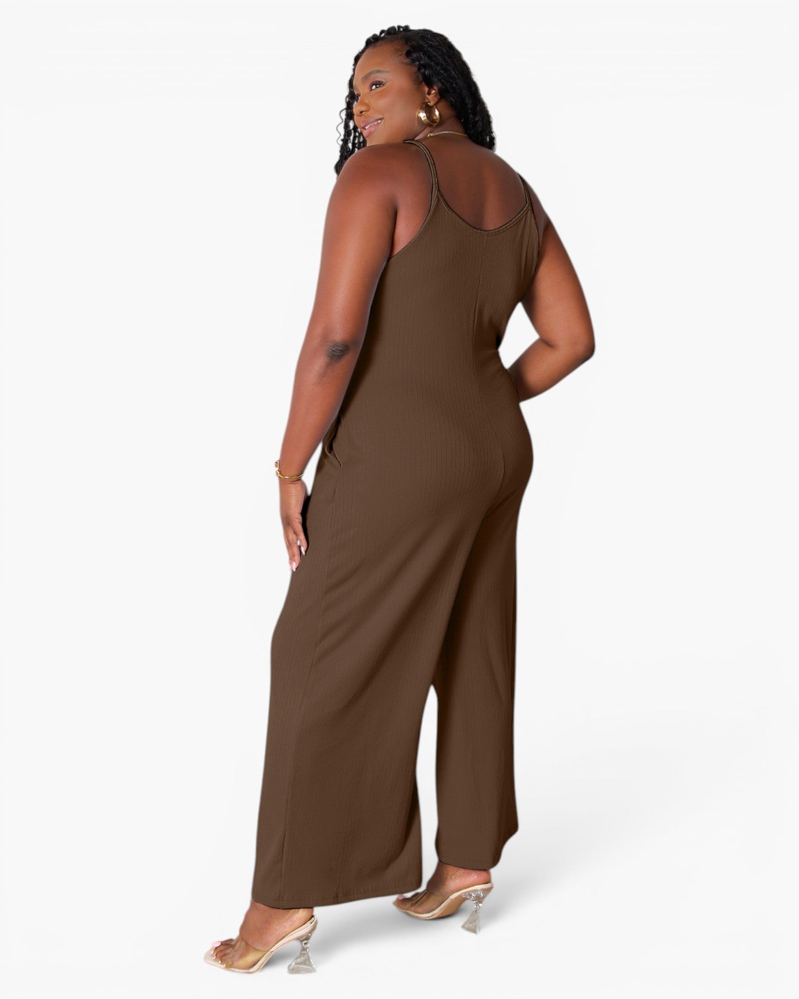 A woman modeling a brown sleeveless jumpsuit from the back, showing a high open back and wide legs, against a plain white studio background.