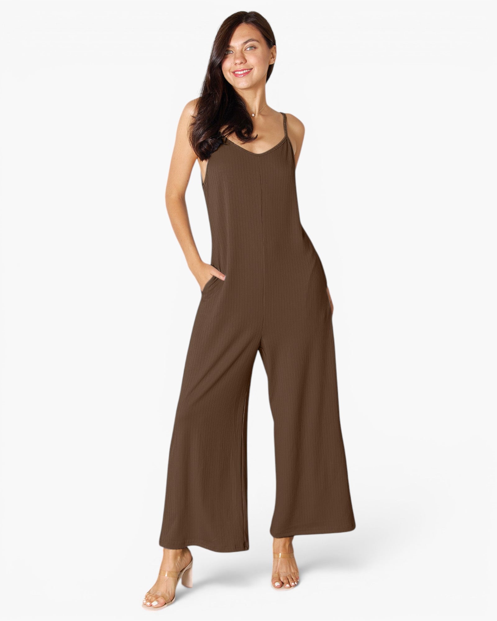 A woman modeling a sleeveless wide-leg jumpsuit in a solid dark brown color, standing against a clean white studio background.