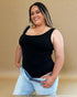 Woman wearing a black tank top and light blue jeans against a beige background