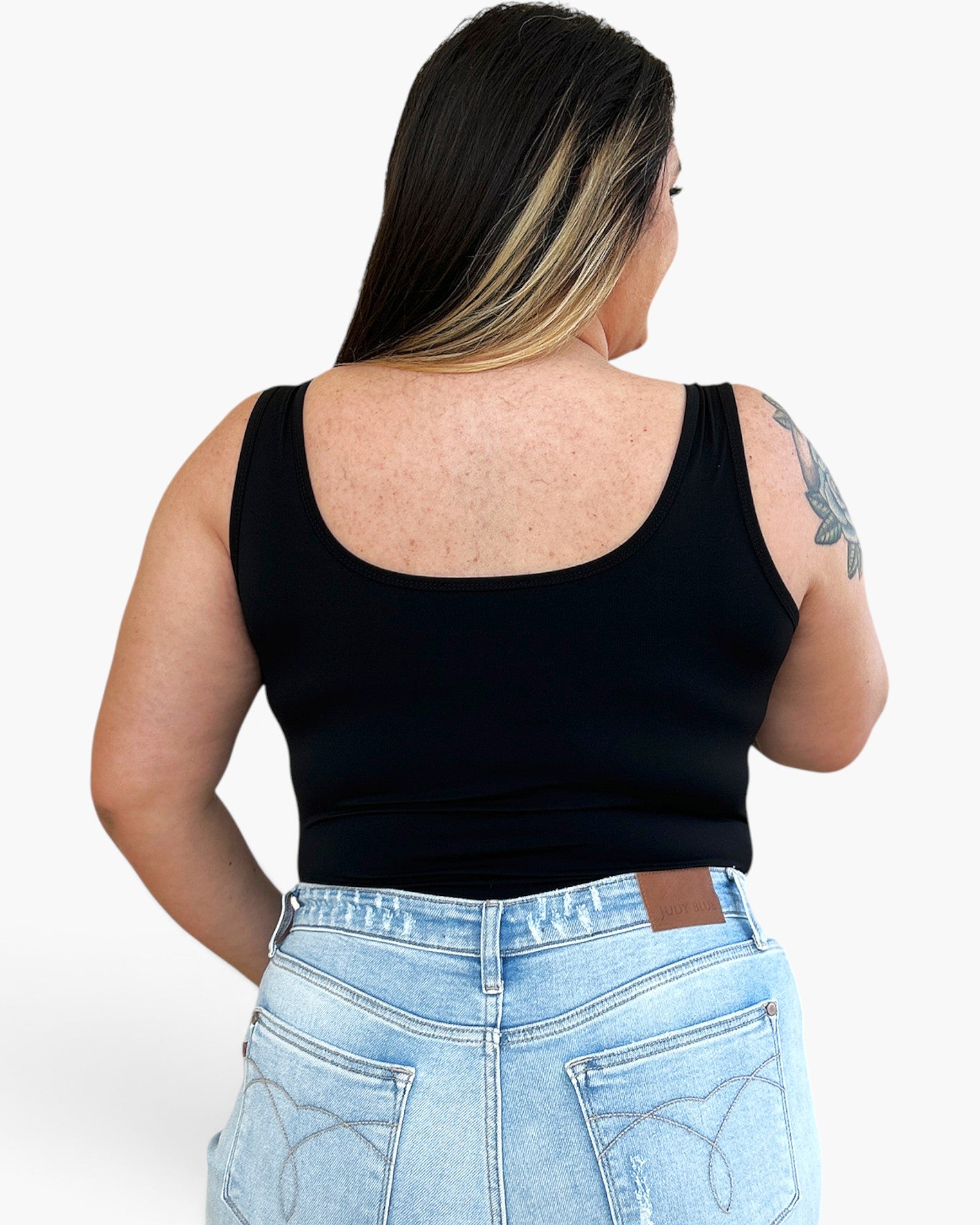 A woman shown from the back wearing a black scoop-neck tank top and light blue jeans against a plain white background.