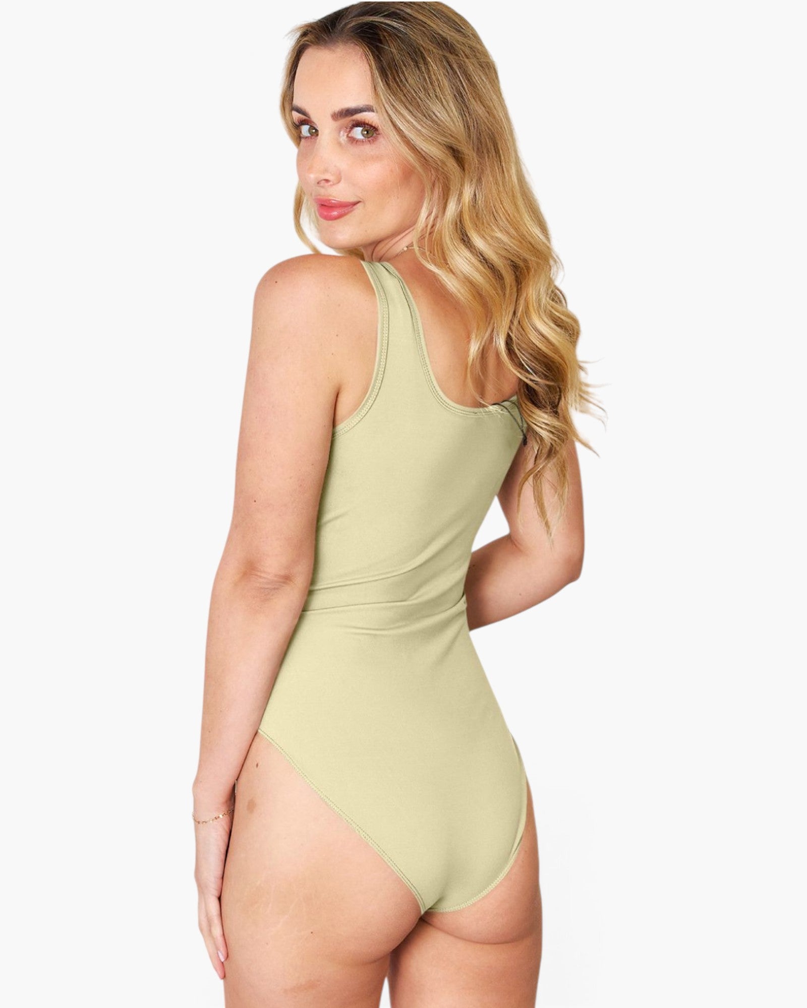 A woman modeling a light sage green one-piece swimsuit from the back, shown against a plain light gray studio background.