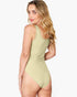 A woman modeling a light sage green one-piece swimsuit from the back, shown against a plain light gray studio background.