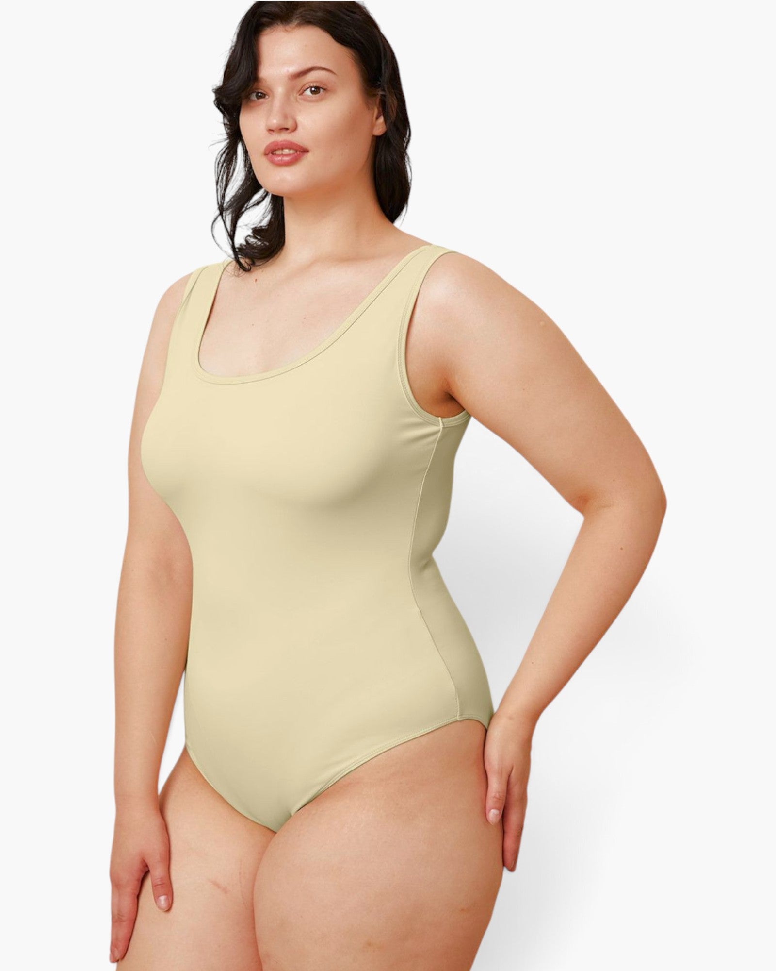 A woman modeling a light beige one-piece swimsuit against a plain light gray studio background.