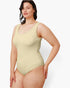 A woman modeling a light beige one-piece swimsuit against a plain light gray studio background.