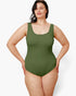 A woman modeling a sleeveless one-piece swimsuit in olive green against a plain light gray studio background.