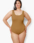 A woman modeling a sleeveless scoop-neck one-piece swimsuit in a solid tan color, posed against a light gray studio background.