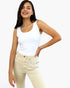 A woman modeling a fitted white scoop-neck tank top paired with light beige jeans, set against a plain light gray studio background.