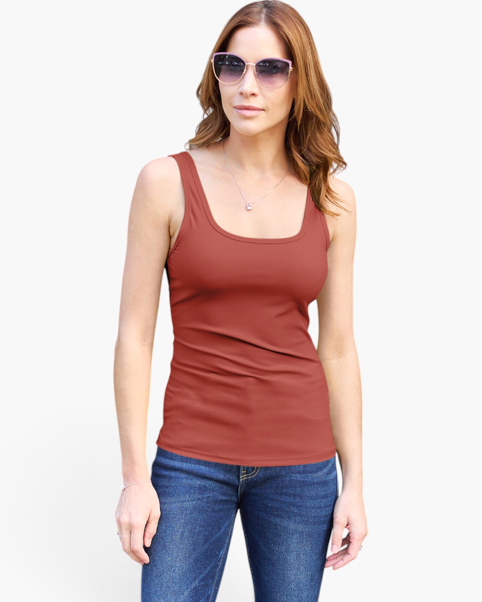 A woman modeling a rust-colored scoop-neck tank top with blue jeans and sunglasses against a plain white background.