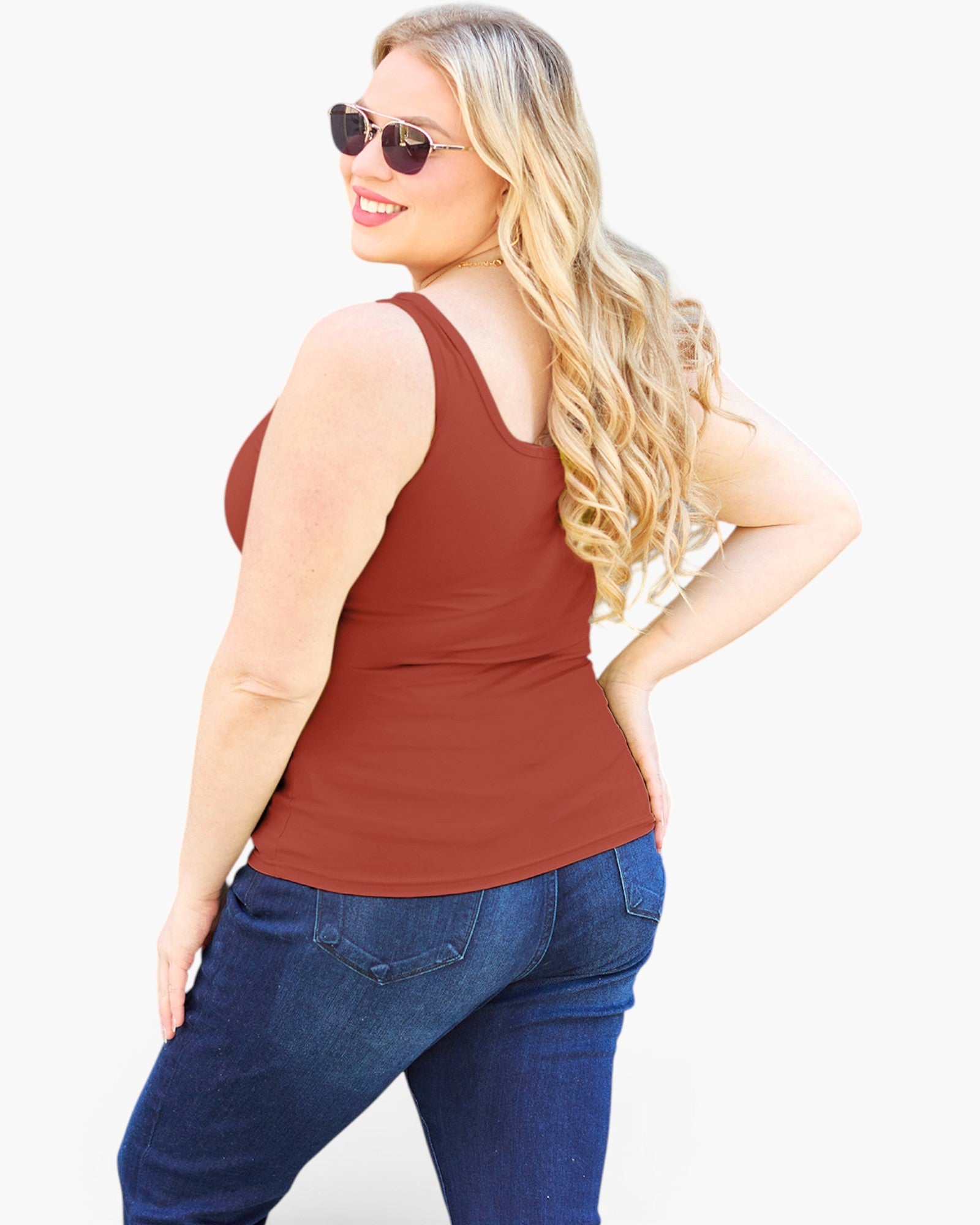 A woman with long blonde hair and sunglasses, wearing a rust-brown ribbed tank top and blue jeans, shown from a back-three-quarter angle against a plain white background.