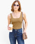 A woman modeling a fitted tan tank top with blue jeans, sunglasses, a crossbody bag, and a coffee cup, photographed against a plain light background.