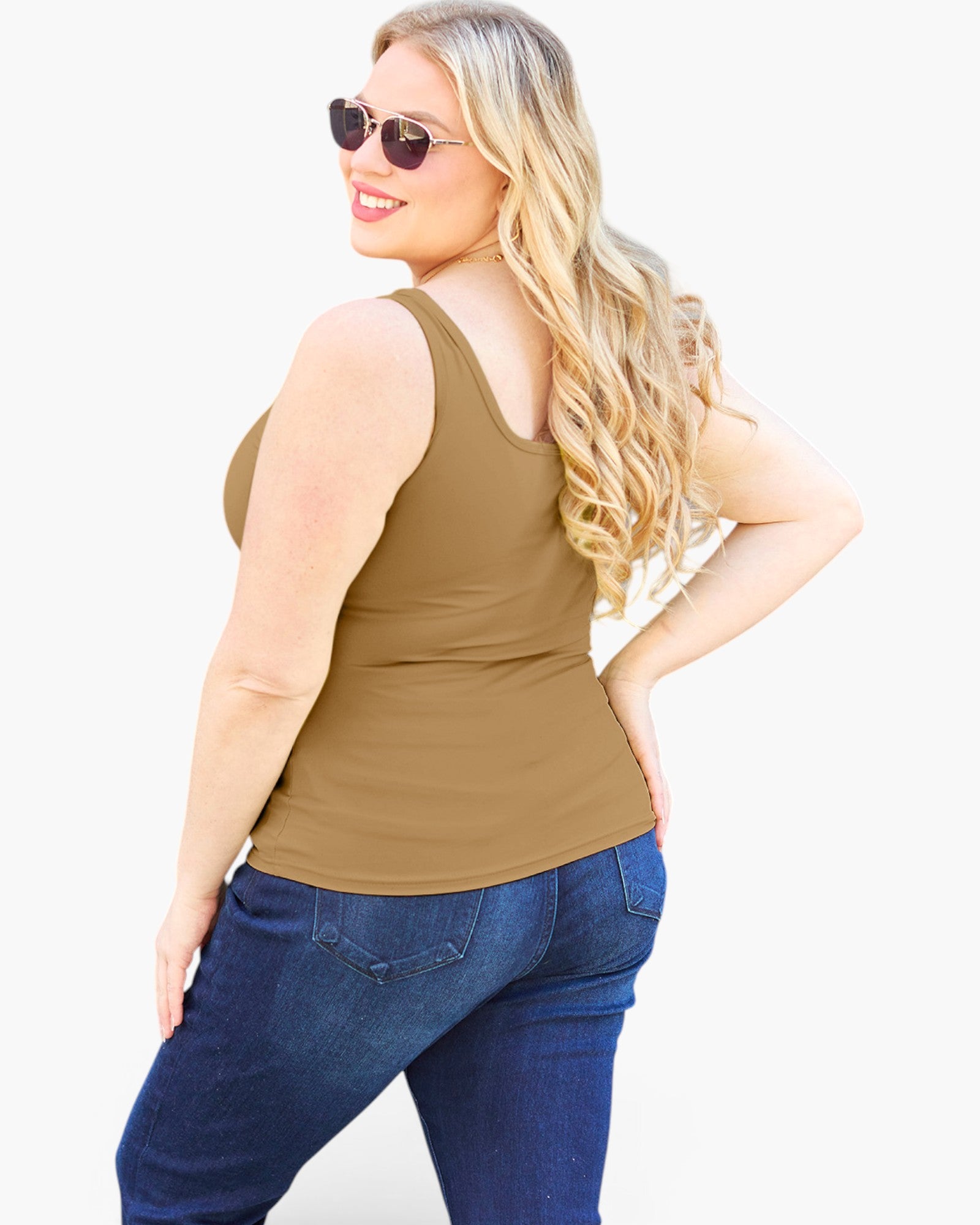 A woman modeling a fitted sleeveless tank top in a warm taupe-brown color, paired with dark blue jeans, photographed against a clean white studio background.