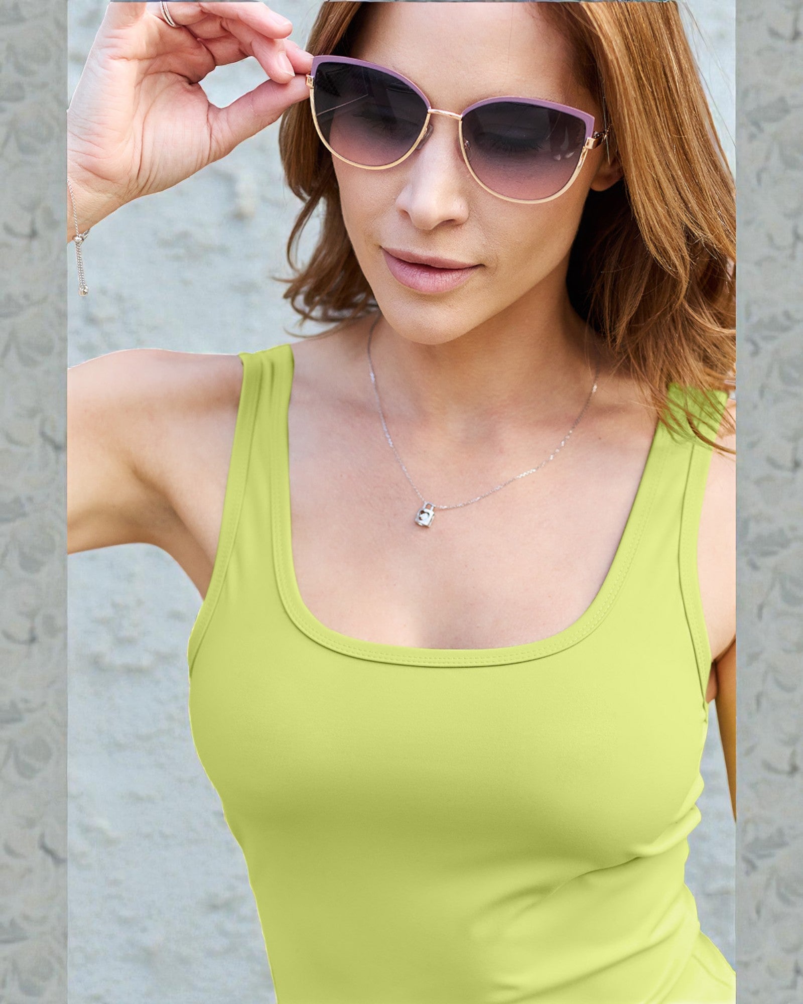 Woman wearing a green tank top and pink sunglasses against a neutral background