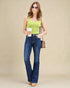 Woman wearing a green tank top and blue jeans, holding a coffee cup and a handbag on a beige background