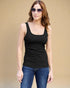 Woman wearing a black tank top and blue jeans against a beige background