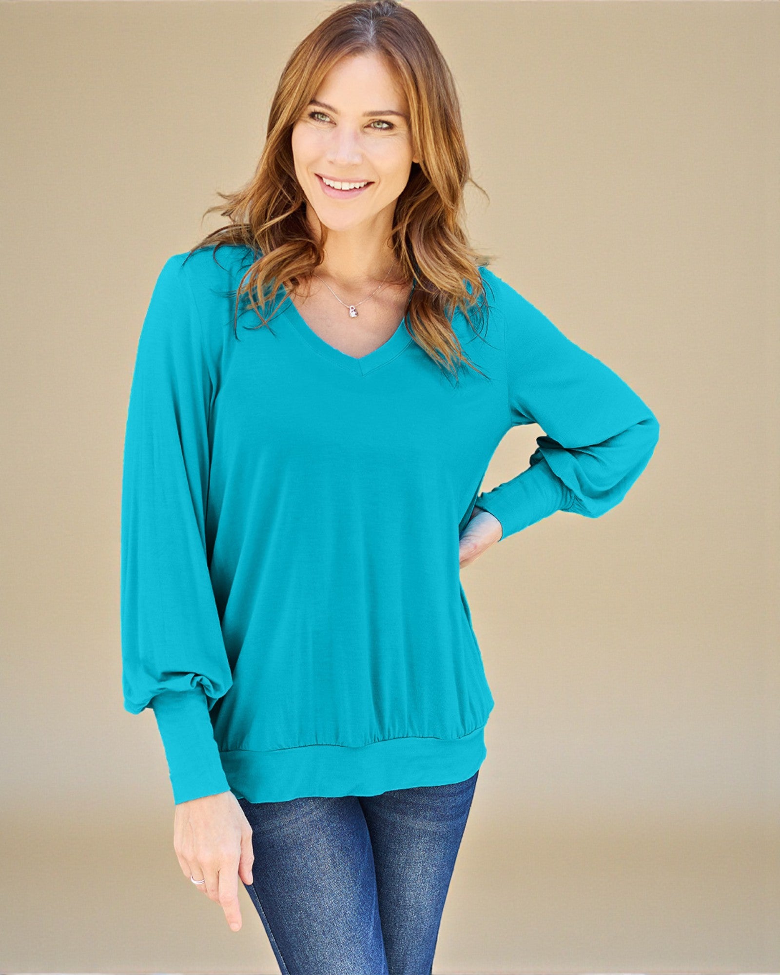 Woman wearing a teal sweater and jeans on a beige background