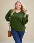 Woman wearing a green sweater and blue jeans against a beige background