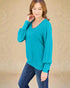Woman wearing a teal long-sleeve top against a beige background
