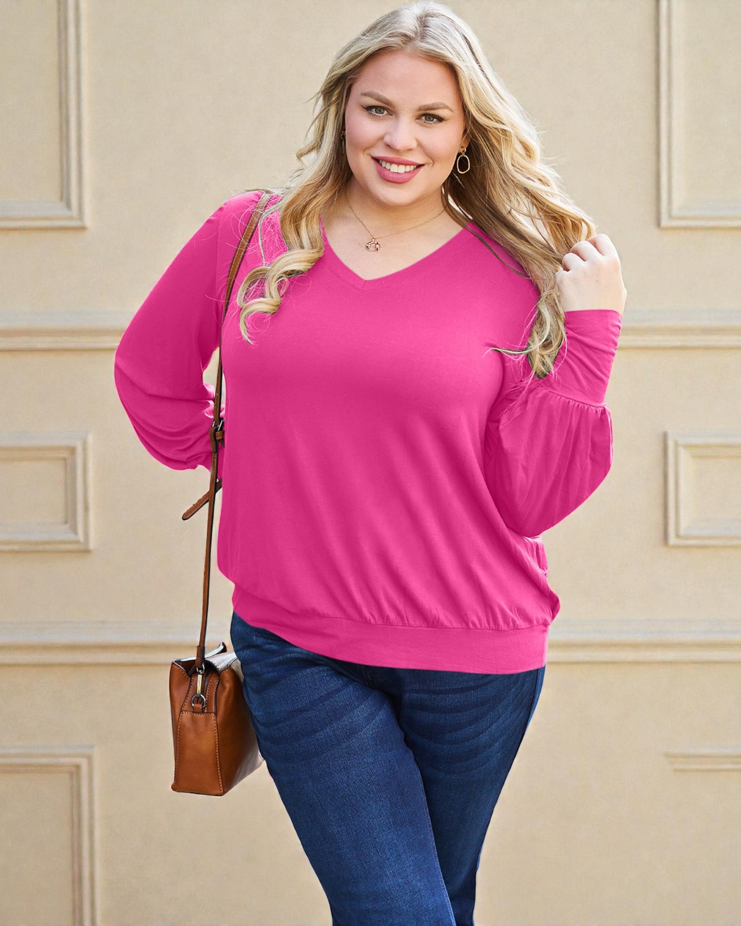 Woman wearing a bright pink long-sleeve top and blue jeans against a beige wall.